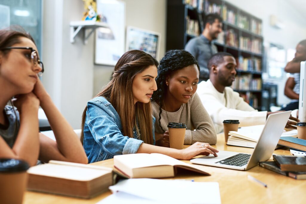 Shot of two young students using a laptop together in a college library