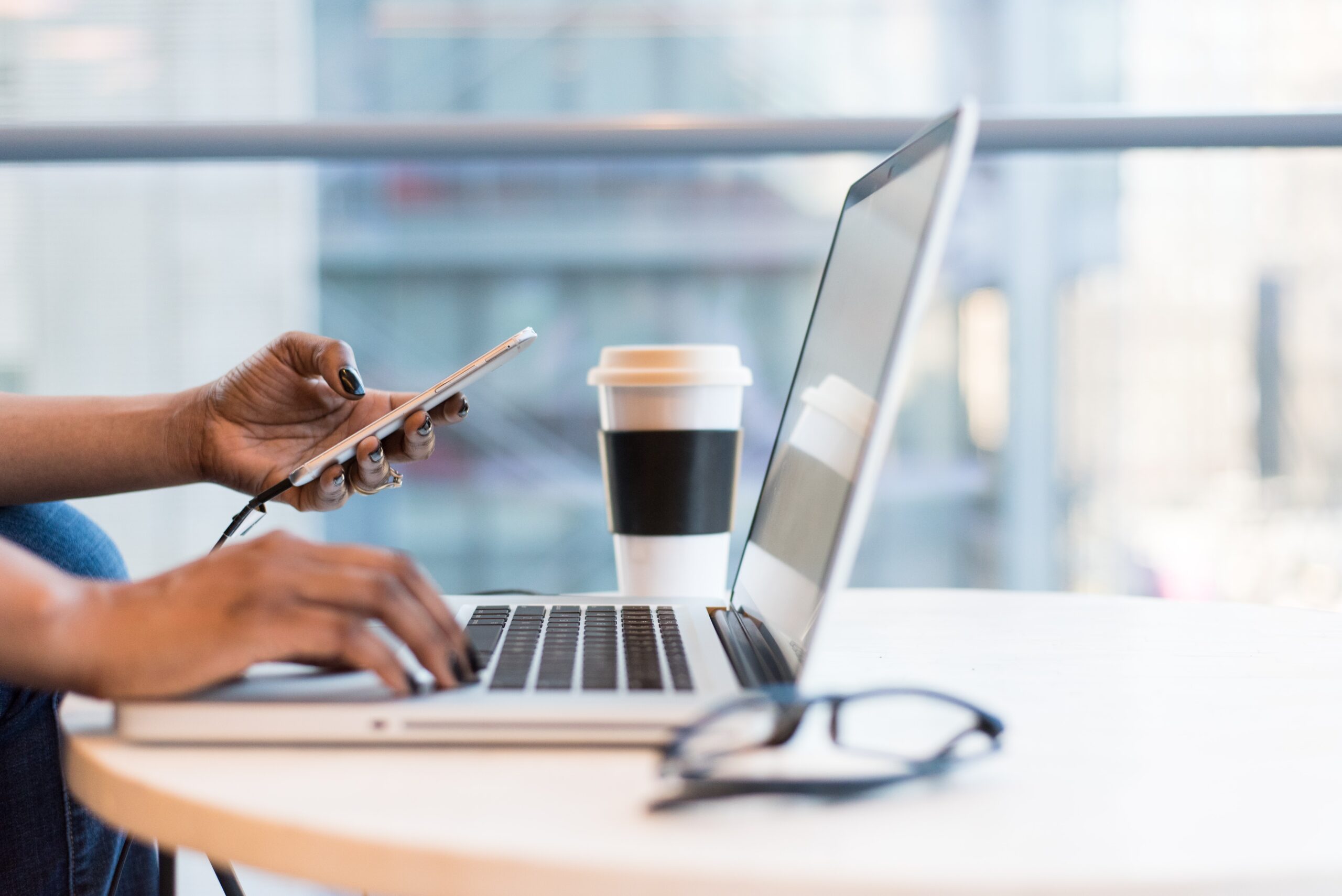 Person's hand holding a mobile phone whilst typing on laptop applying for university via UCAS